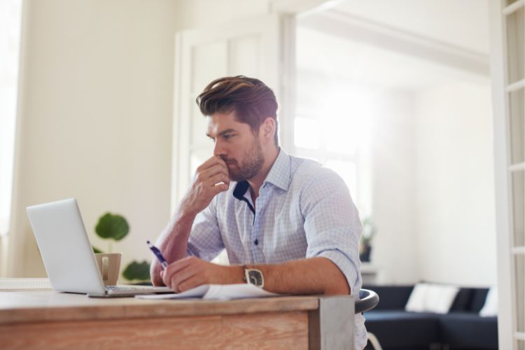 Small business leader engaged in focused planning, seated at a desk with a laptop and notebook in a bright, modern workspace. The thoughtful posture and organized setting—with coffee mug, pen, and natural light—reflect strategic thinking and a commitment to growth and decision-making.